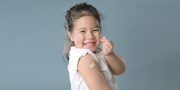 menina com um curativo de vacina no braço sorrindo e fazendo um coração com os dedos